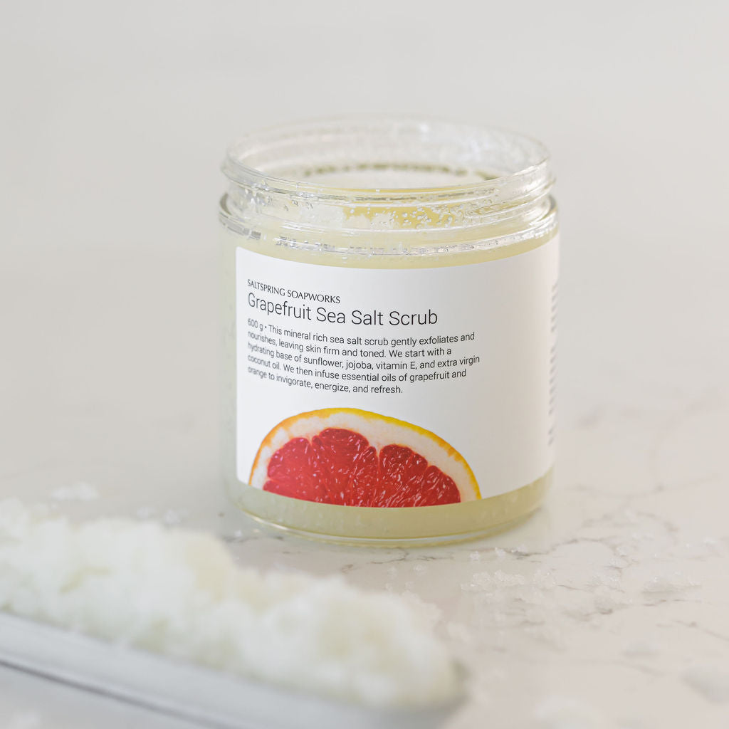 Jar of grapefruit sea salt scrub with a white label on a light gray background