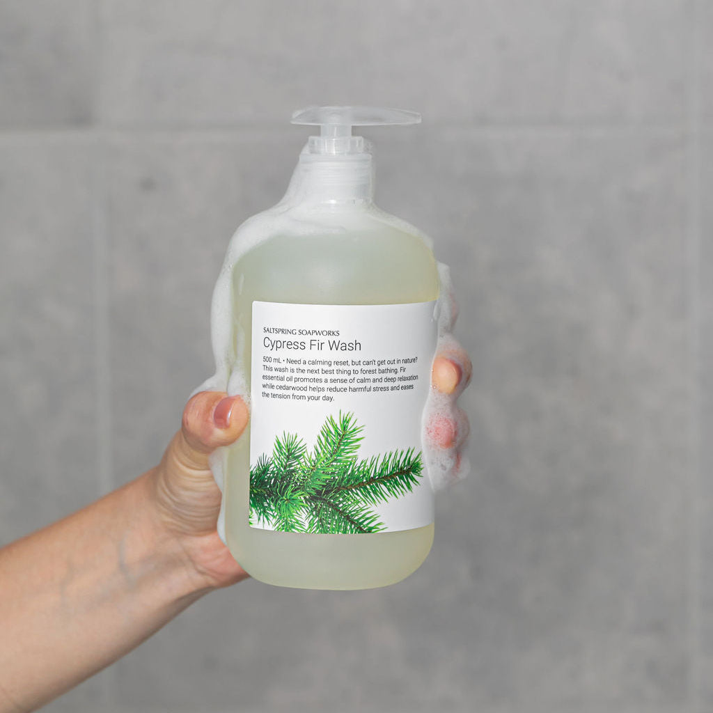 Hand holding a bottle of Cypress Fir Wash against a gray background
