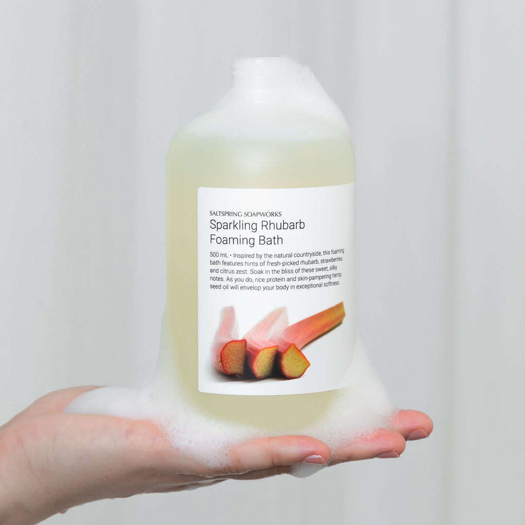 Hand holding a bottle of foaming bath with rhubarb flavor against a white background
