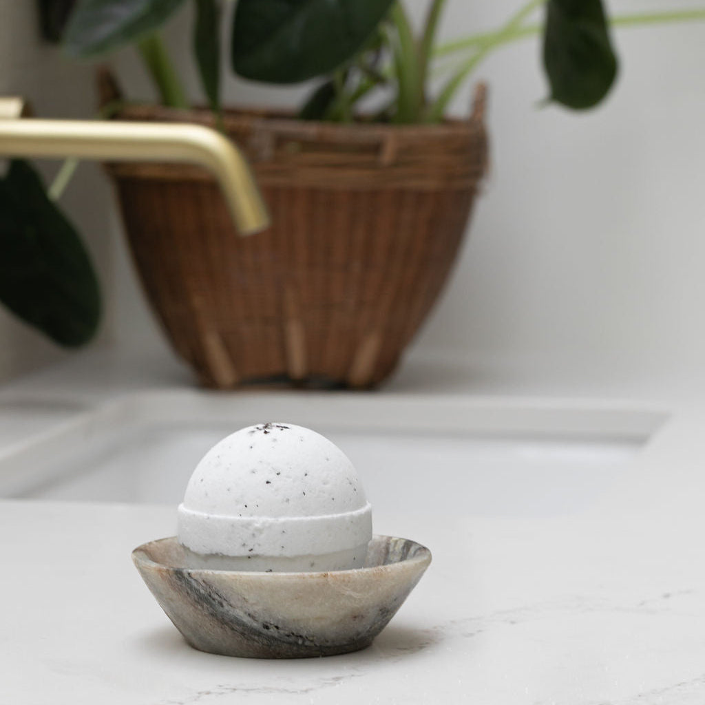 Saltspring Soapworks Cedar Eucalyptus bath bomb in a decorative stone holder on a marble surface with a plant in the background.