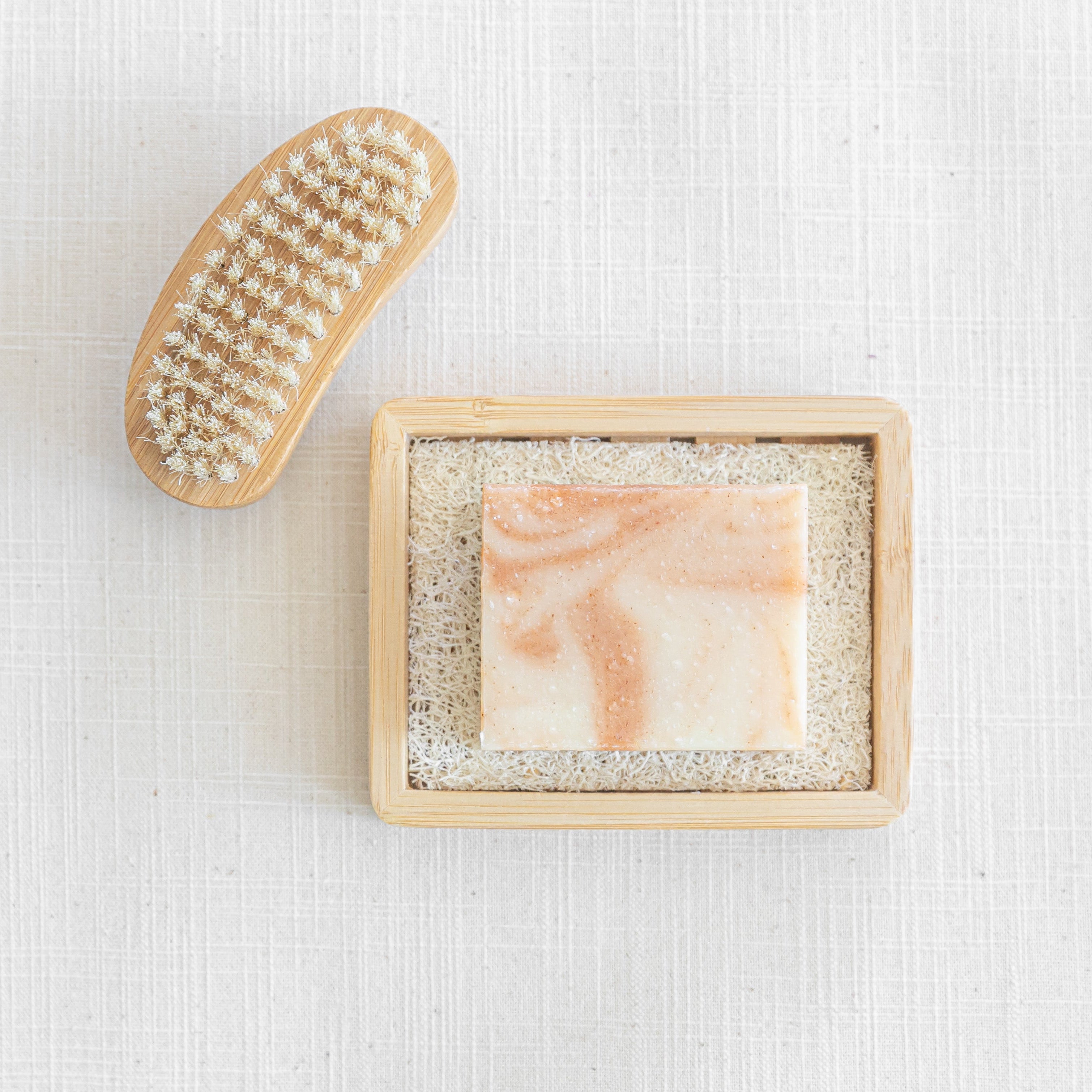 Small scrub brush and soap bar with swirls on a wooden holder on a textured white background