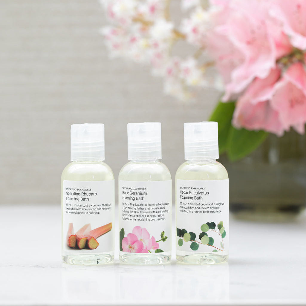 Set of three Saltspring Soapworks foaming bath bottles, travel sized, including Sparkling Rhubarb, Rose germanium and Cedar Eucalyptus with floral background