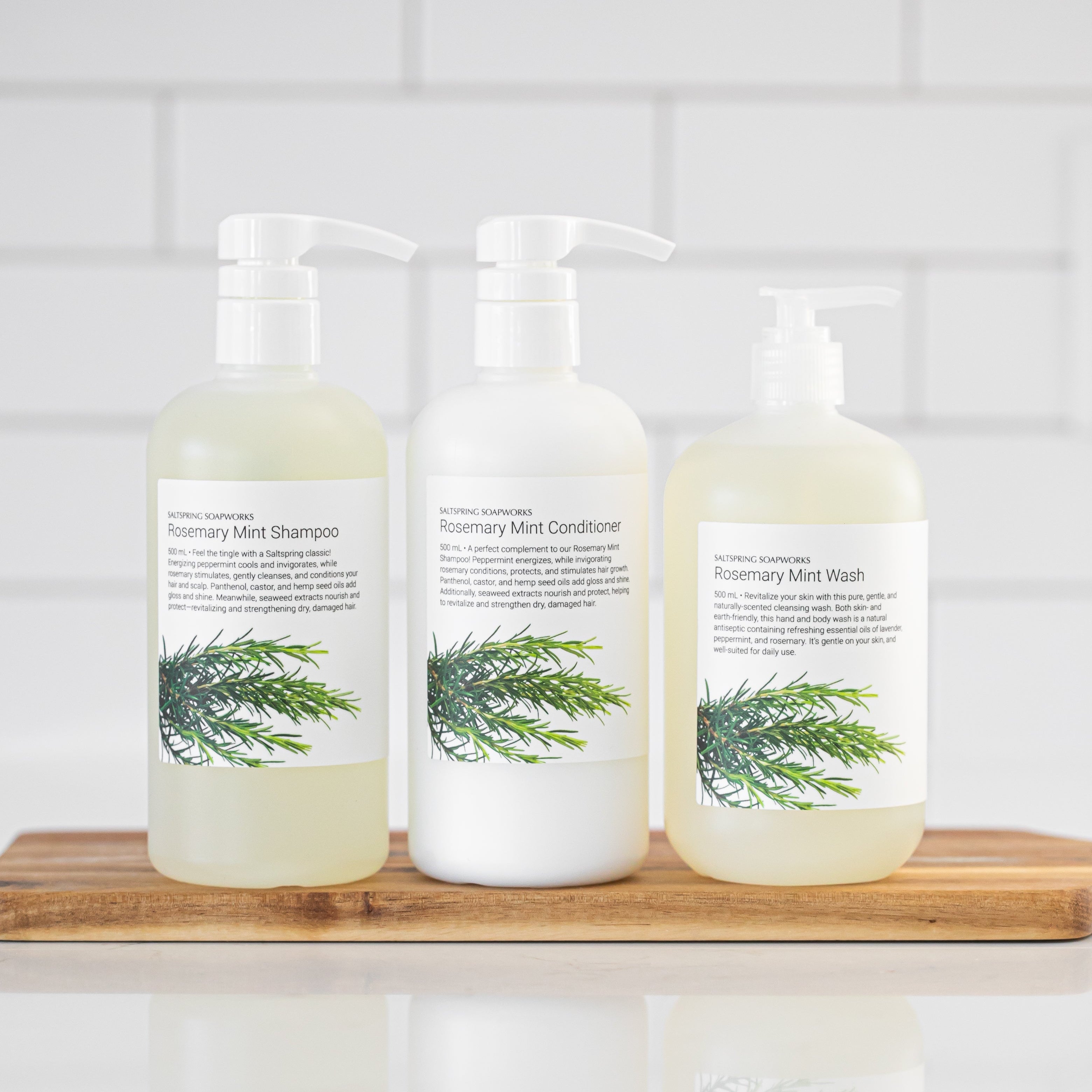 Three bottles including shampoo, conditioner, and wash on a wooden board with a white tiled background