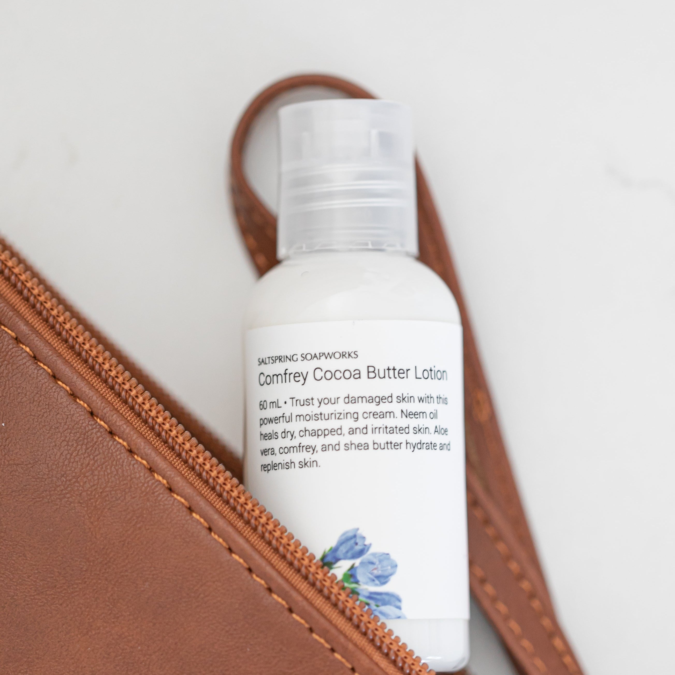 White bottle of lotion in a brown leather pouch on a white background