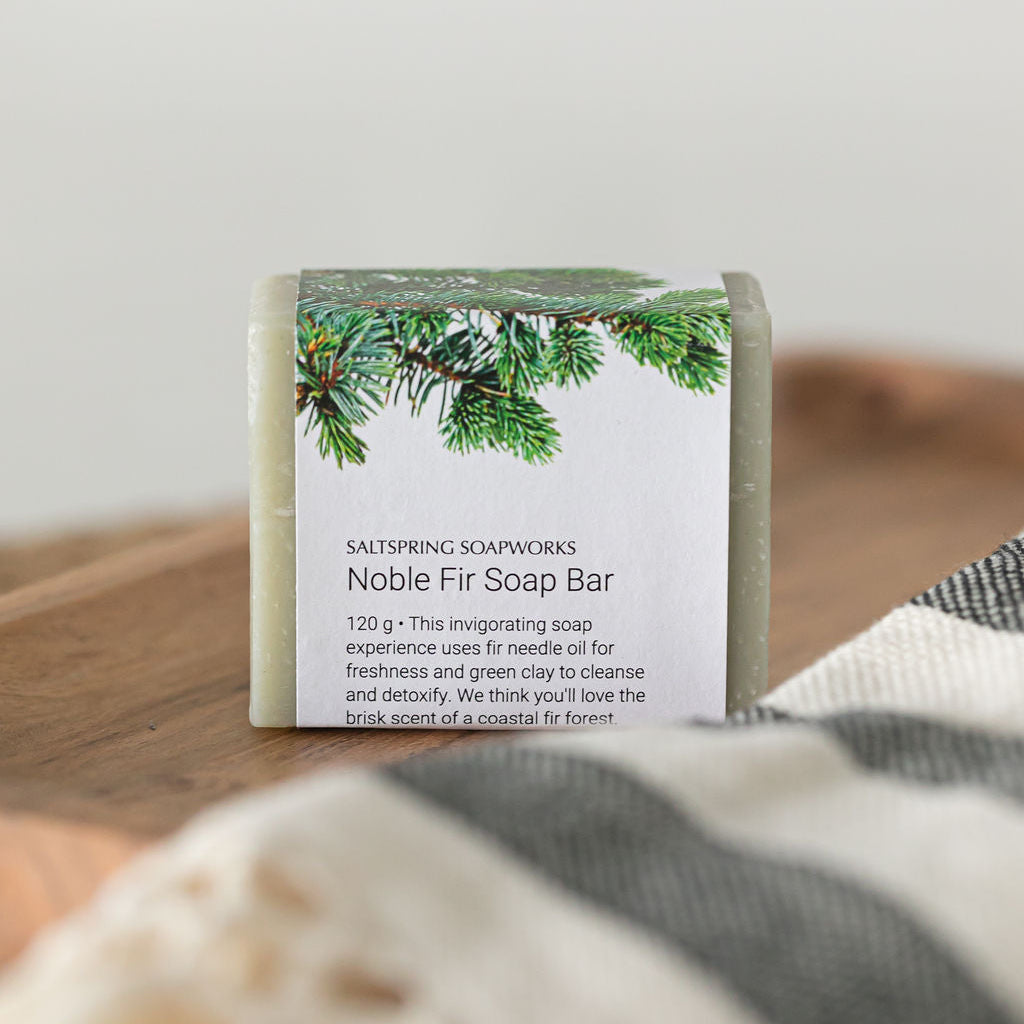 Saltspring Soapworks Noble Fir Soap Bar with illustrated fir branch label on wooden surface.