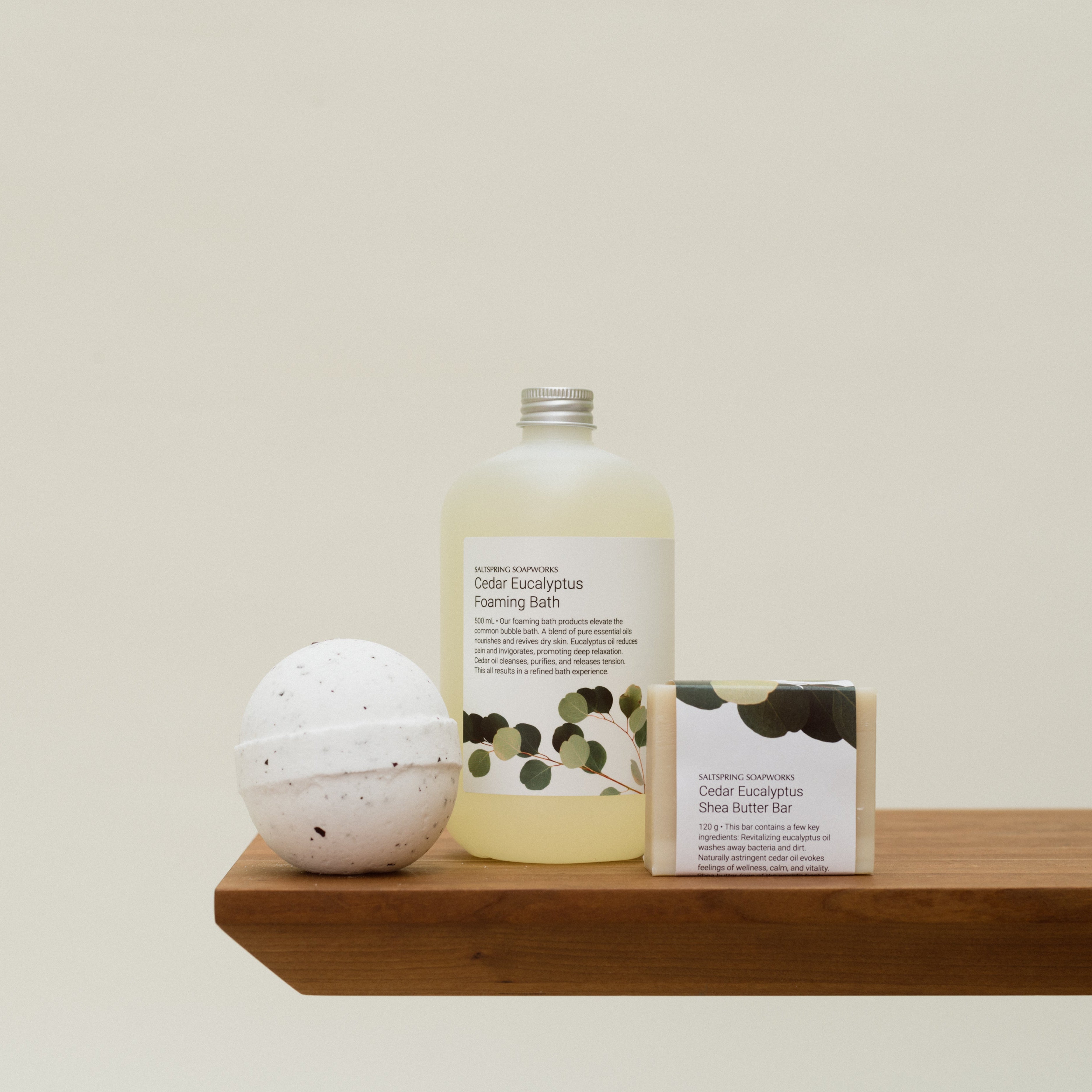 Bottle, bath bomb, and soap on a wooden shelf against a beige background