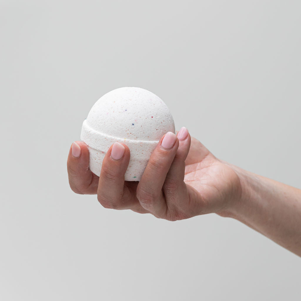 Hand holding Saltspring Soapworks Candied Grapefruit bath bomb against a light gray background