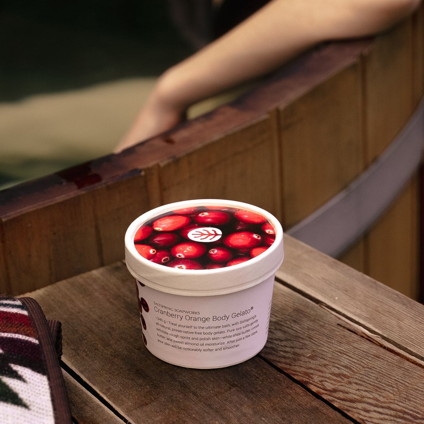 Jar of Cranberry Orange Body Gelato on a wooden surface with blurred wood hot tub in background
