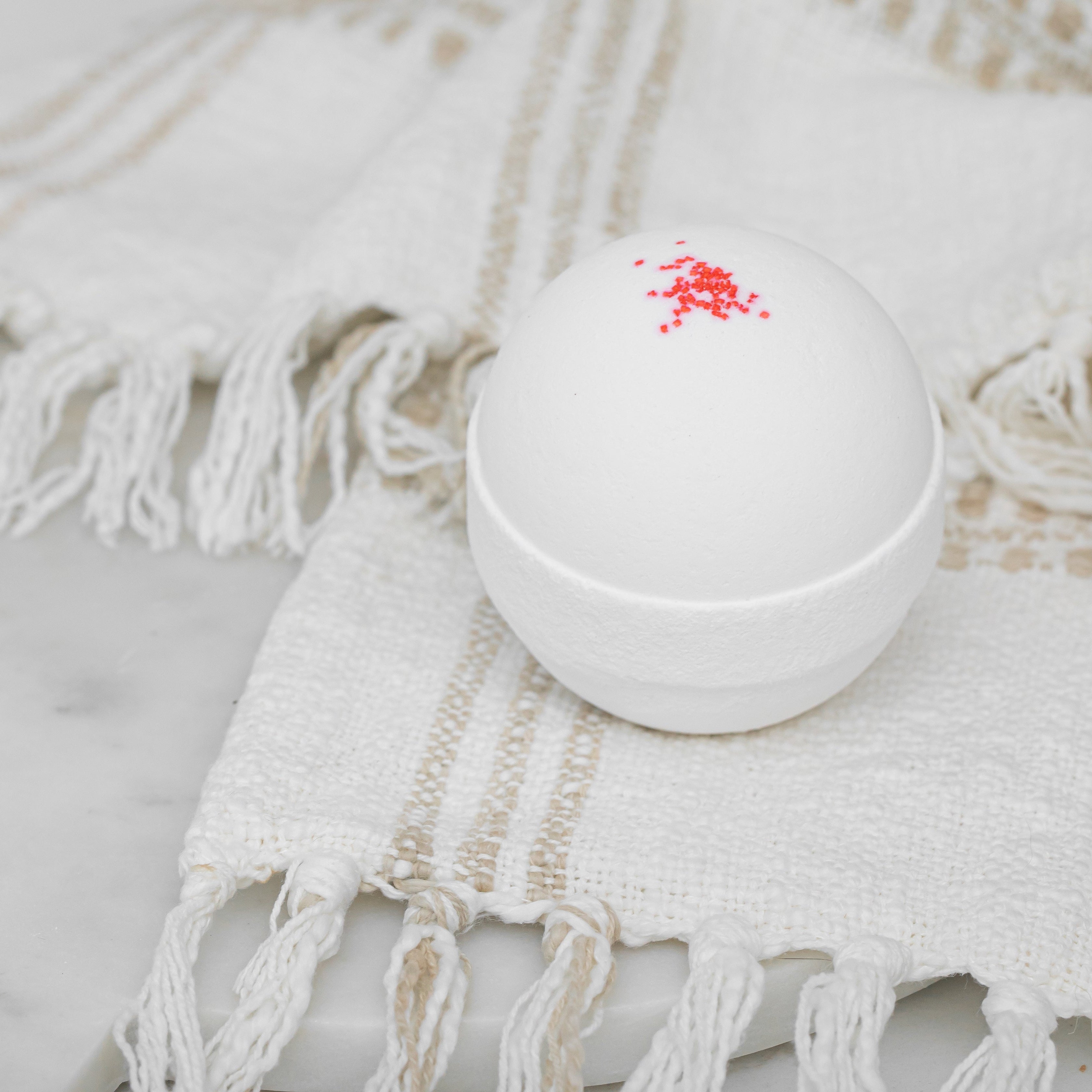 white bath bomb with red sprinkles on cloth with tassles
