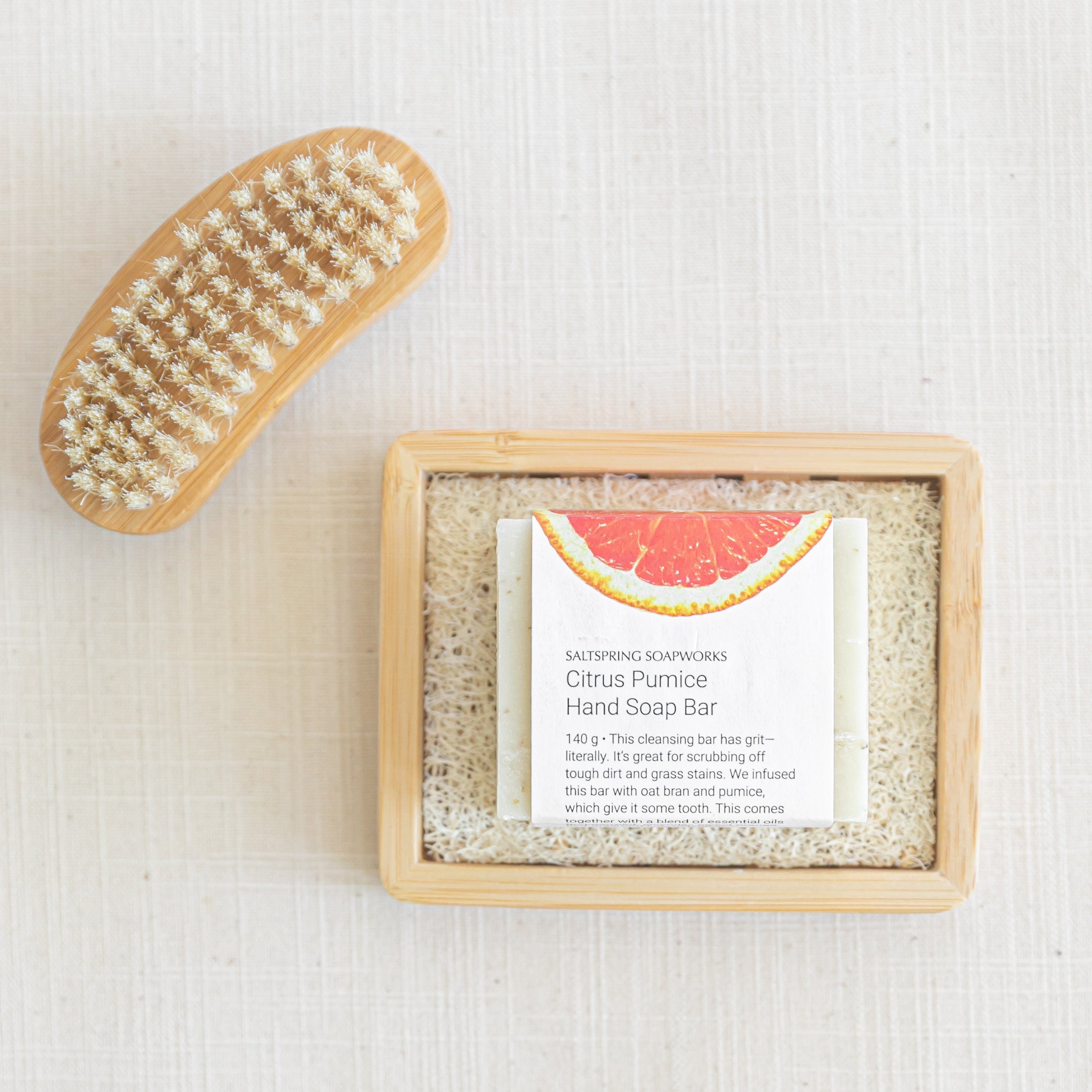 Hand soap bar with a wooden tray and a brush on a textured white background