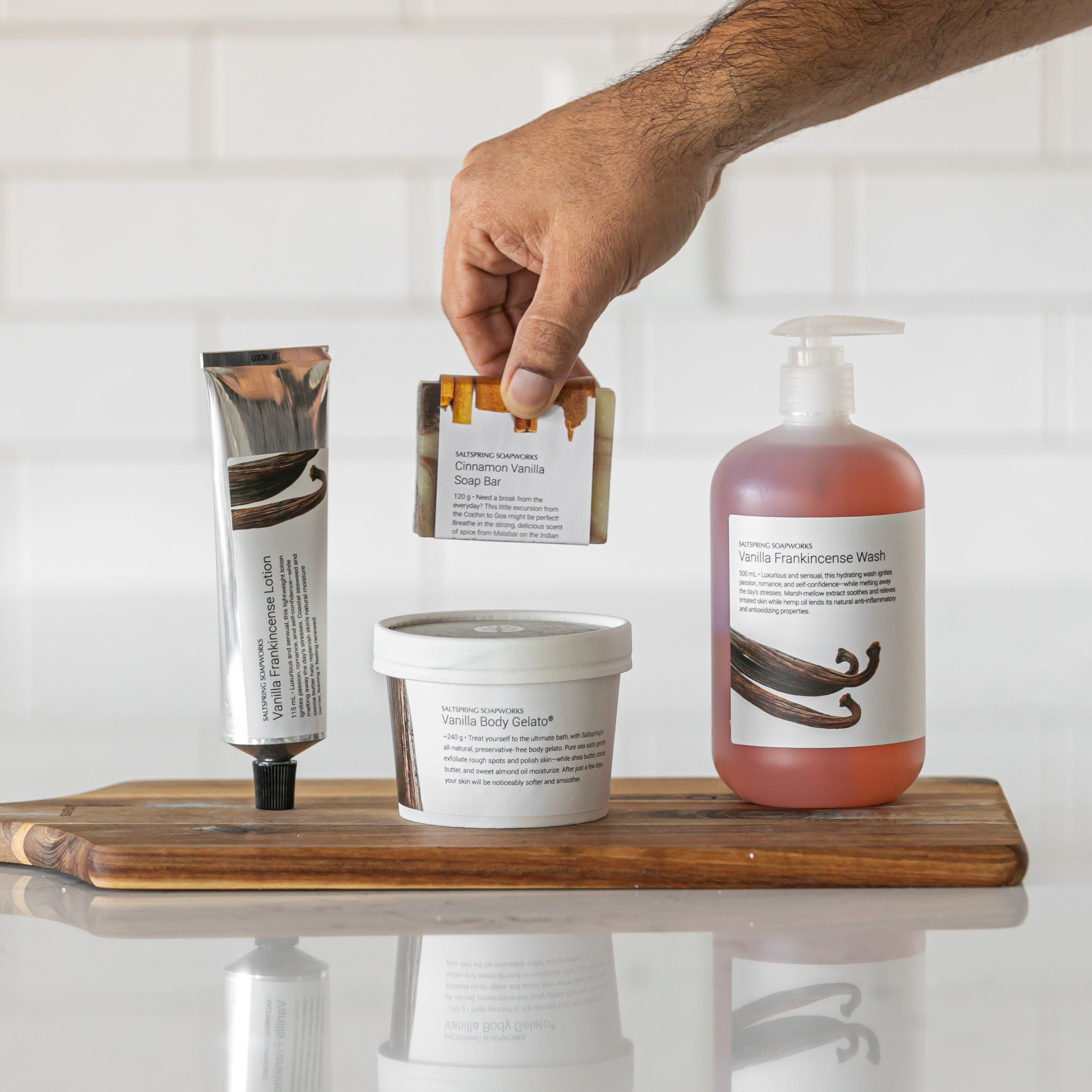 Hand reaching for a soap bar on a wooden tray with various skincare products.