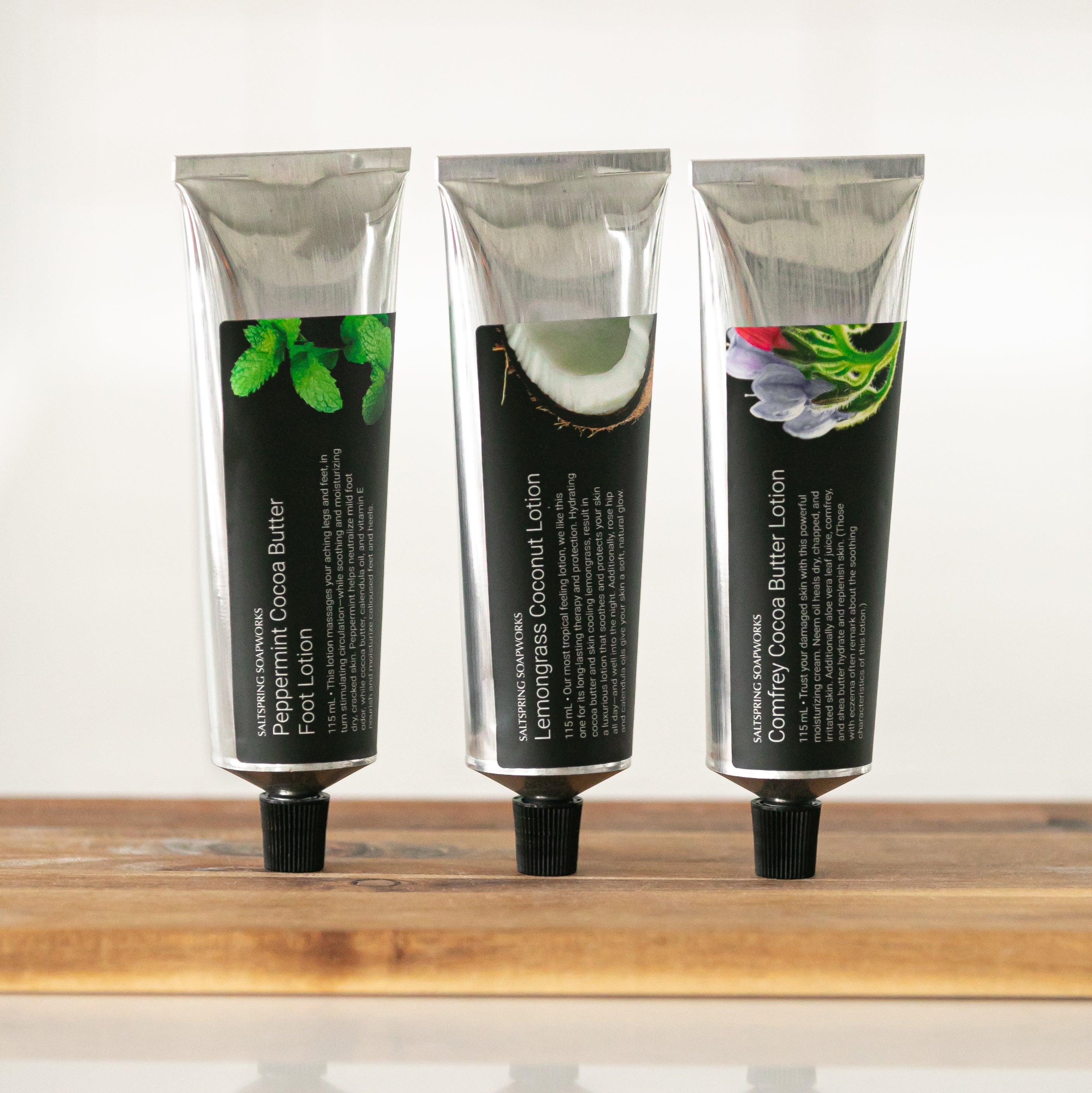 Three tubes of hand lotion on a wooden shelf with a white background