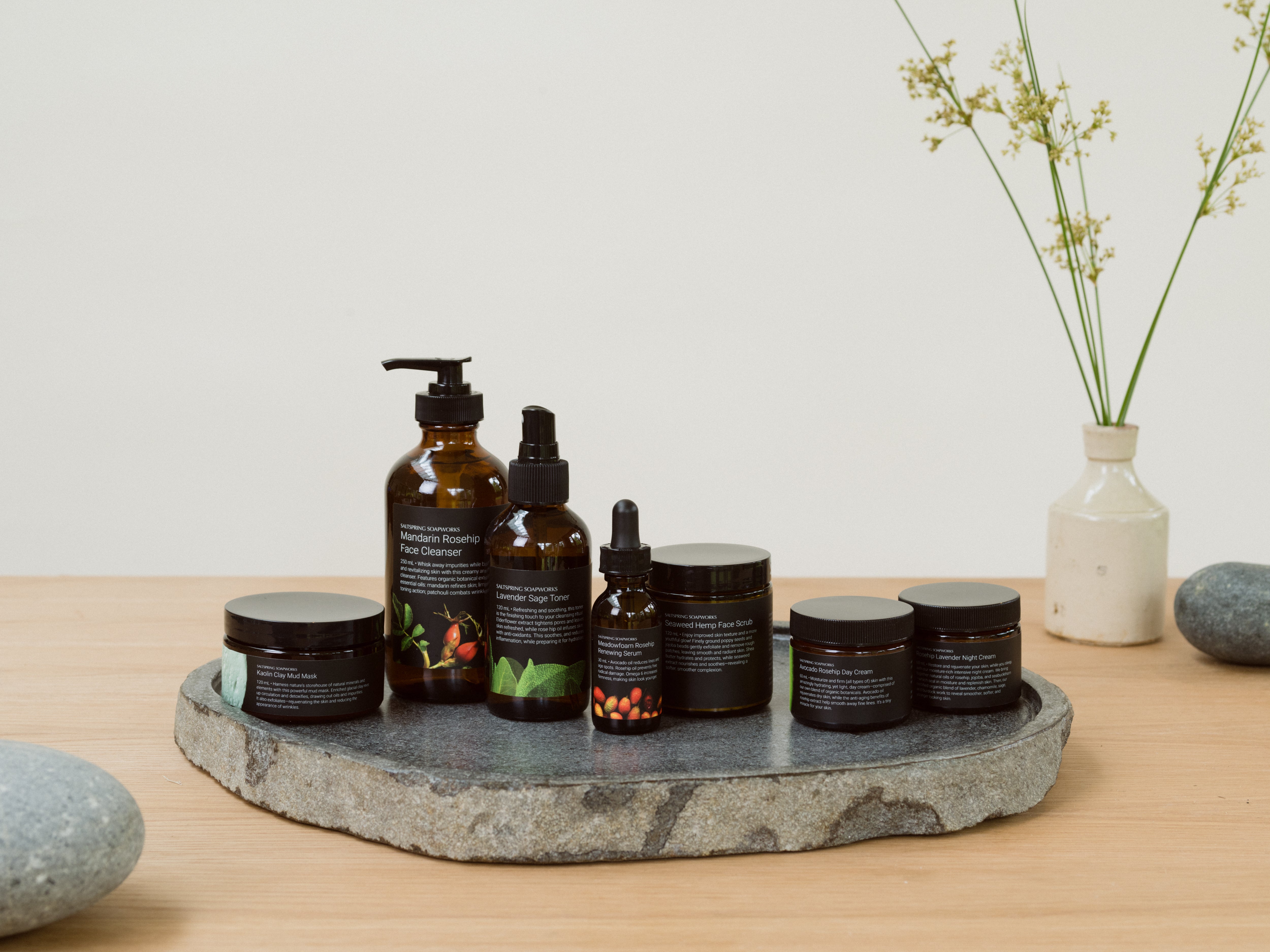 Saltspring Soapworks complete skincare collection displayed on a stone slab including Mandarin Rosehip Face Cleanser, Lavender Sage Toner, Meadowfoam Rosehip Serum, Seaweed Hemp Face Scrub, Kaolin Clay Mud Mask, Rosehip Day Cream, and Lavender Night Cream